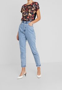 Černý top s květinovým vzorem, krátké rukávy, zkombinovaný s džíny světle modré barvy s vysokým pasem. Bílé špičaté lodičky dokončují outfit.