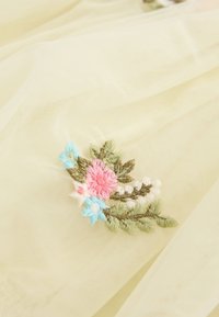Délicate broderie de fleurs roses, bleues, blanches et de feuilles vertes sur un tissu doux, translucide, beige clair.