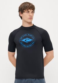 Svart rash guard med kort ärm, tillverkad av sträckbart material, med en blå cirkulär logotyp som har "Rip Curl Surf Co" och "Established 69."