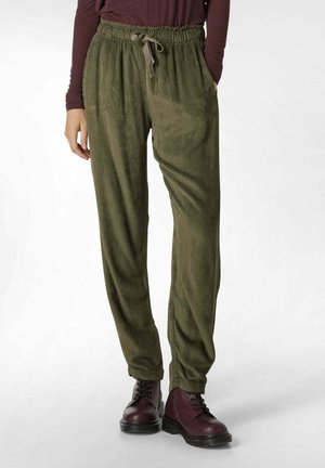 Green corduroy pants with a relaxed fit, elastic waistband, drawstring detail, side pockets, and tapered legs; paired with burgundy boots.