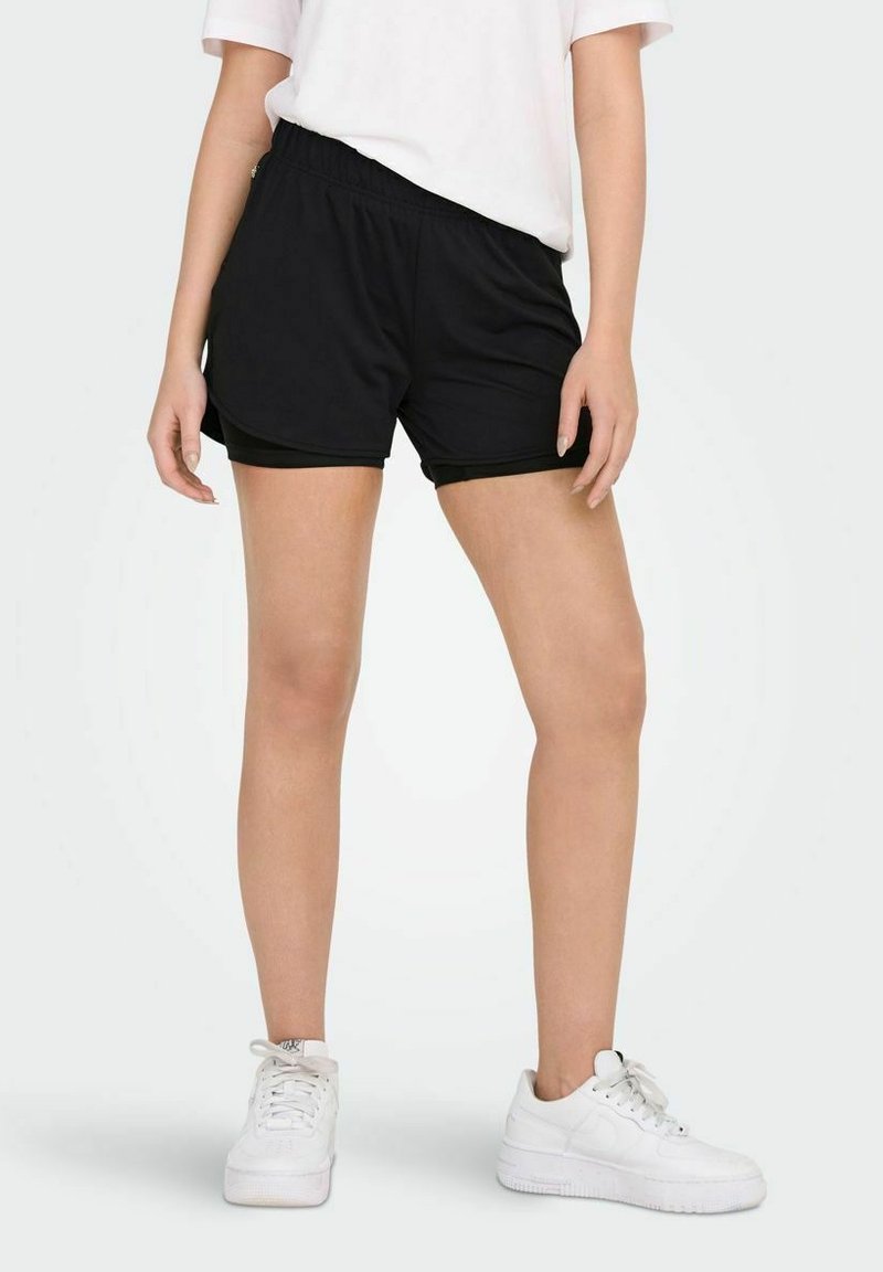 Black athletic shorts with an elastic waistband, featuring a smooth texture and contrast seams, worn with white sneakers.