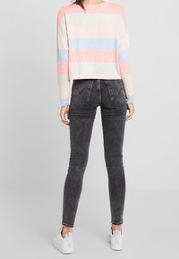 Lehký, krátký svetr se pruhy v růžové, modré a krémové barvě; spárovaný s černými džínami vysokého pasu a bílými teniskami na slip.