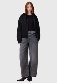 Sudadera negra con capucha y detalles de botones, combinada con jeans grises de corte holgado y dobladillo deshilachado. Botines negros de punta.