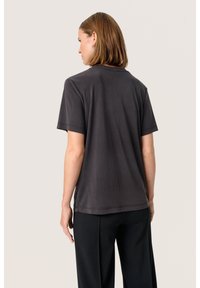 Tricou scurt gri închis cu un croi lejer. Textură netedă și decolteu rotund. Design simplu, fără modele sau elemente metalice vizibile.