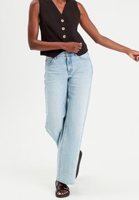 Haut noir sans manches avec trois grands boutons, associé à un jean taille haute bleu clair et des sandales noires avec une boucle d écorative.