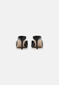 Mules noires en cuir verni à talon haut avec un dos ouvert, présentant un design élégant et un talon aiguille effilé, sur un fond neutre.