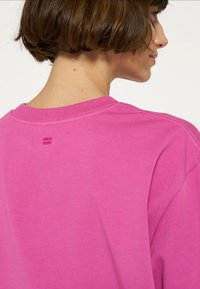 T-shirt in cotone rosa con scollo tondo, dettagli di cucitura visibili e un piccolo dettaglio sulla parte posteriore del collo. Tessuto morbido e vestibilità comoda.