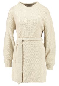 Stickad tröja i ljusbeige med ett mönster, vida ärmar och ett matchande bälte i midjan. Har en hög krage.