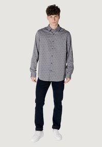 Camisa gris de botones con un patrón sutil, de manga larga, con cuello y bolsillo en el pecho, combinada con jeans oscuros y zapatillas blancas.