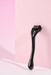 Zwarte dermaroller met een glad handvat, voorzien van een rollerkop met fijne, kleine naalden, rustend tegen een roze achtergrond.