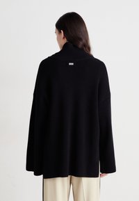 Schwarzer Strickpullover mit hohem Kragen und lockerer Passform. Verfügt über weite Ärmel, gerippte Textur und ein kleines Markenschild auf der Rückseite.