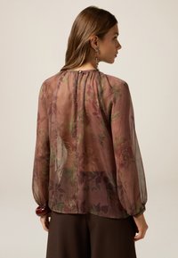 Transparente Blumenshirt in burgunder und grün, mit langen Ärmeln und gerafftem Halsausschnitt. Verfügt über einen kleinen Knopfverschluss im Rücken.