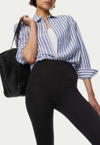 Blå och vit randig skjorta med knappar, långa ärmar, kombinerad med svarta högmidjade leggings och en vävd svart tote-väska.