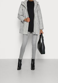 Szary płaszcz w jodełkę z kapturem, czarny golf, szare obcisłe jeansy, czarne skórzane botki za kostkę oraz czarna torebka. Gładkie tekstury.