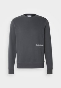 Sweat-shirt gris foncé à manches longues avec un petit logo Calvin Klein blanc sur le bas à droite, doté de poignets et d'un ourlet côtelés.