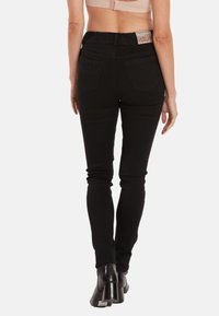 Jeans skinny en denim noir avec une taille haute. Caractéristiques de poches arrière et de détails de couture subtils. Portés avec des bottines à talons noires.