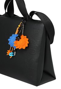 Zwarte tas met een gestructureerd ontwerp, voorzien van een getextureerd materiaal. Accessoires omvatten blauwe en oranje gehaakte bloemen en een zwart berenbedeltje.