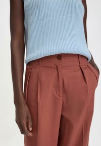 Vaaleansininen neuletankki, johon on yhdistetty ruosteenväriset laskostetut housut, joissa on sivutaskut ja etunapit.