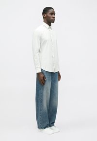 Leicht gestreiftes Hemd mit Knöpfen und Kragen, kombiniert mit weit geschnittenen, ausgewaschenen blauen Jeans und weißen Turnschuhen. Einfaches, modernes Design.