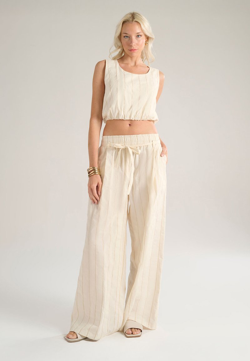 Completo in lino a due pezzi composto da un top corto senza maniche con righe verticali e pantaloni a gamba larga con vita elastica in un colore beige chiaro.