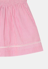 Růžová a bílá pruhovaná látka, která má smockovaný pas a dekorativní prošívání podél lemu. Texturovaný bavlněný materiál.