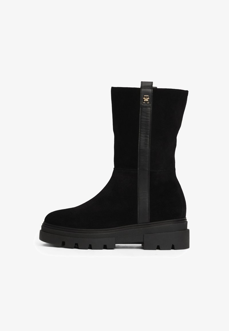 Bottines noires en daim et cuir. Présentent une semelle épaisse avec une texture rugueuse et une bande en cuir vertical avec un accent en métal doré.