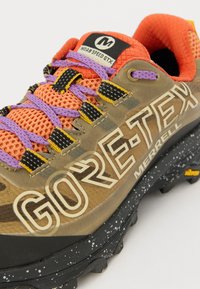 Brune GORE-TEX vandresko med mesh-detaljer, lilla, orange og sorte snørebånd, samt en plettet sort gummisål. Viser "MERRELL" branding.