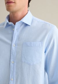 Lichtblauwe button-up shirt gemaakt van zacht materiaal, met een puntkraag, een opgestikte zak aan de voorkant en witte knopen langs de sluiting.