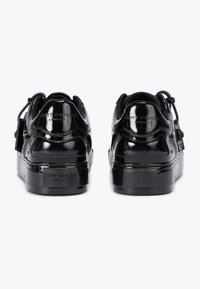 Un paio di sneakers nere lucide con il marchio "Kurt Geiger London" sul tallone, viste dal retro su uno sfondo bianco.