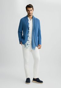Blaues Blazer, weißes Hemd mit Palmenmuster, gestreifter Schal, weiße Hose und marineblaue Schuhe. Glatte Texturen und taillierte Passform.