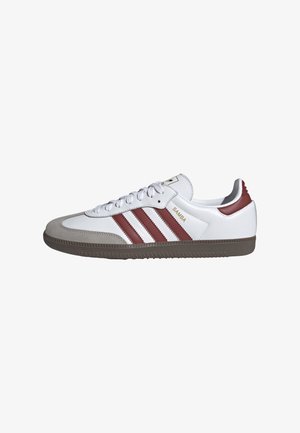 Białe niskie tenisówki Adidas Samba z bordowymi paskami, szarą zamszową nakładką na palce, brązową podeszwą i sznurówkami na białym tle.