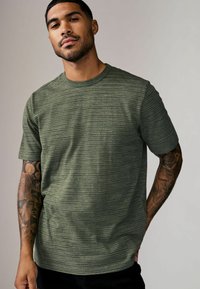 Tricou scurt cu mânecă, de culoare verde măsliniu, dintr-un material texturat, având guler rotund și dungi orizontale subtile pe suprafață.