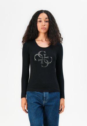 Zwart shirt met lange mouwen en een ronde halslijn, voorzien van een glanzend grafisch ontwerp in het midden. G gedragen met blauwe spijkerbroek.
