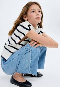 Stickad ärmlös tröja med marinblå ränder, ljusblå vida jeans med fransad nederkant och svarta ballerina skor med en rosettdekoration.
