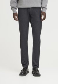 Temno sivi krojeni hlače ožjega kroja, gladke teksture in subtilnim vzorcem. Obuti z črnimi usnjenimi čevlji.