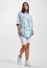Camiseta oversize de flores en tonos azules y blancos con mangas cortas, combinada con pantalones cortos de ciclista blancos y zapatillas blancas.