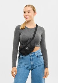 Čierny ľadvinkový batoh so subtilným tónovým vzorom, zakriveným tvarom, predným vreckom na zips a nastaviteľným popruhom noseným cez telo.