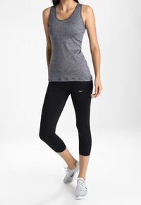 Top senza maniche grigio abbinato a leggings neri (capri). I leggings presentano un piccolo logo e l'outfit è completato da sneakers chiare.