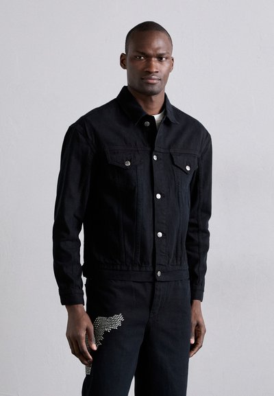 Schwarze Jeansjacke mit zwei Brusttaschen, silbernen Beschlägen und einer Knopfschließe. Die Textur ist glatt; taillierter Schnitt mit einem Kragen.