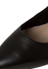 Gros plan d'une chaussure en cuir noir à bout pointu, texture lisse et doublure intérieure beige.