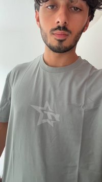 Camiseta de manga corta gris claro con un sutil logo de estrella en un tono ligeramente más oscuro en el pecho, hecha de una tela suave con una textura lisa.