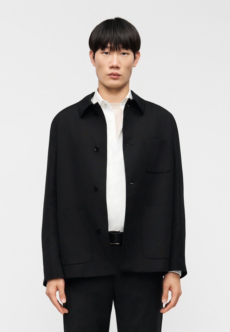 Μαύρο σακάκι με κουμπιά, γιακά, τσέ πη στο στήθος και δύο μπροστινές τσέπες. Σχεδιασμένο με άνετη γραμμή και κατασκευασμένο από απαλό ύφασμα.