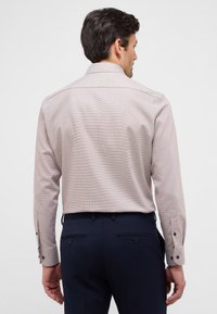Camicia a quadri rosa chiaro con maniche lunghe, polsini abbottonati e colletto classico, abbinata a pantaloni blu scuro.