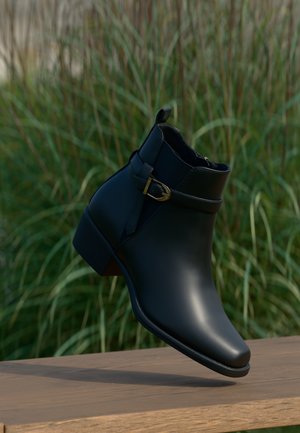 Bottine en cuir noir avec une sangle à boucle dorée, légèrement surélevée au-dessus d'une surface en bois, avec de l'herbe verte en arrière-plan.