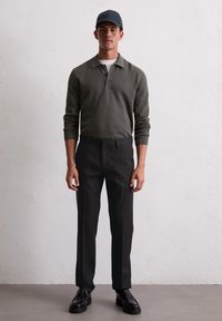 Polo a maniche lunghe di un verde scuro strutturato, pantaloni neri su misura e scarpe eleganti nere. Completato con un berretto scuro. Elementi di design minimal.