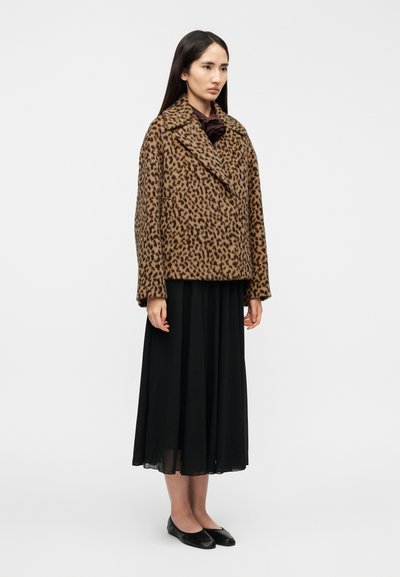 Δίχρωμο σακάκι με σχέδιο λεοπάρ, με ύφασμα που μοιάζει με  γούνα, διπλό πέτο και υπερμεγέθη γιακά. Φορεμένο πάνω από μαύρη, πιετέ φούστα μέχρι το πάτωμα και μαύρα παπούτσια.