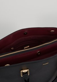 Borsa a tracolla nera in finta pelle con hardware oro, dotata di un interno in tessuto bordeaux, tasca con zip e chiusura magnetica.