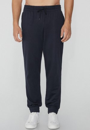 Pantalones jogging azul marino hechos de una tela suave, con una cinturilla elástica, cierre de cordón y puños acanalados. Combinados con zapatillas blancas.