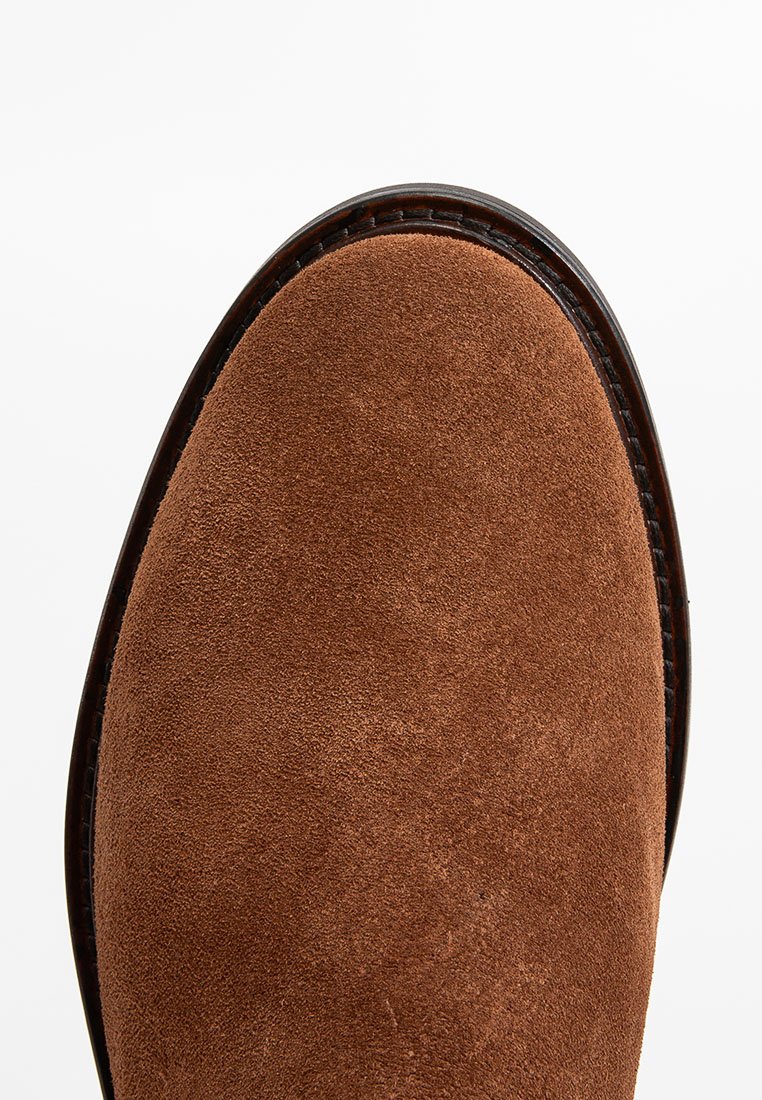Brązowe zamszowe buty z gładkim, okrągłym czubkiem i przeszyciami wzdłuż skórzanej podeszwy, prezentujące miękką fakturę.