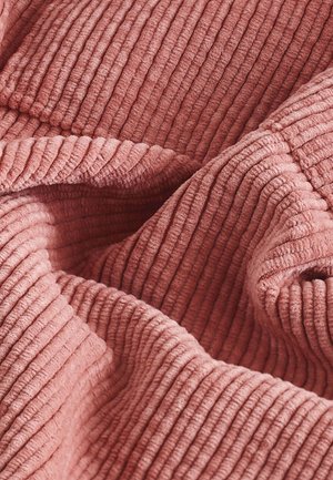 Teksturowana tkanina w delikatnym różowym kolorze z pionowymi żebrowanymi wzorami, prezentująca przytulny i zachęcający wygląd. Materiał ma pluszową, dotykową jakość.